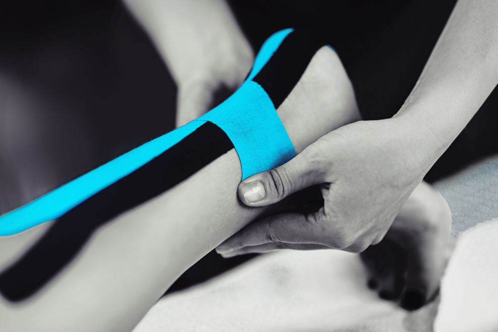 Black and white image of kinesiology taping treatment with blue tape on female patient injured Achilles tendon. Sports injury kinesio treatment.